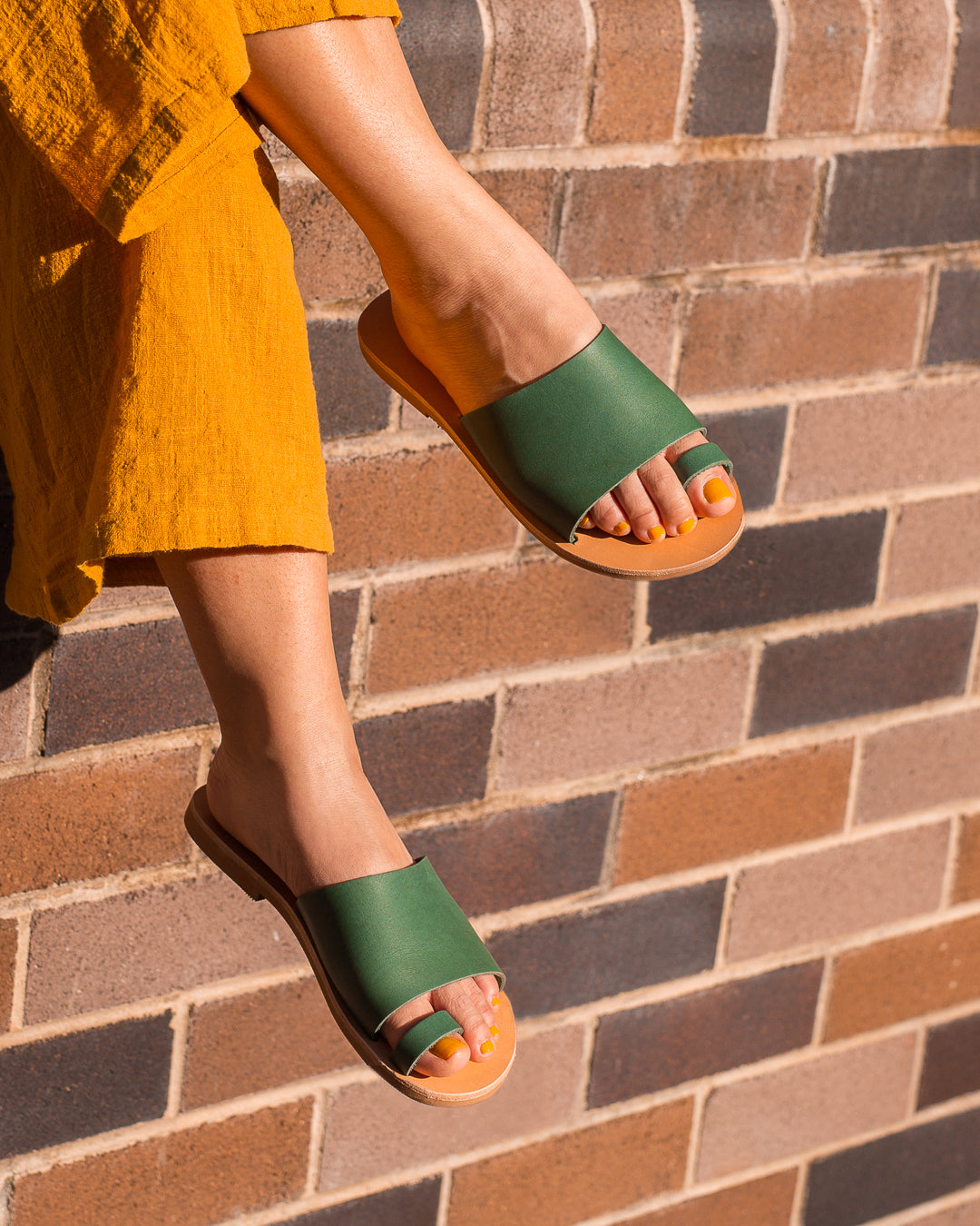 EvieG sandals Beta in green feet wearing the sandals while the girl is seating 